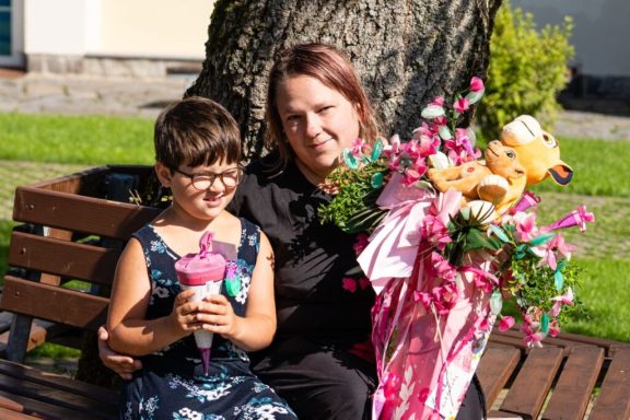 Mädchen mit Eis und Frau mit Blumensträußen und Stofftieren auf einer Bank.