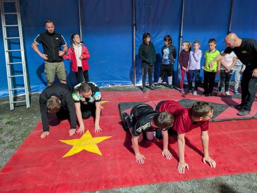 Drei Kinder machen Liegestütze auf einer roten Matte vor einer Gruppe von Zuschauern.