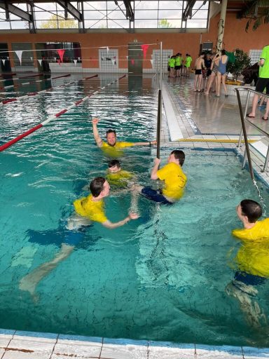 Menschen in gelben T-Shirts haben Spaß im Schwimmbecken. Einige spielen im Wasser.