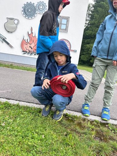Ein Junge in blauer Jacke hockt mit einer roten Rolle auf dem Boden, umgeben von anderen Kindern.