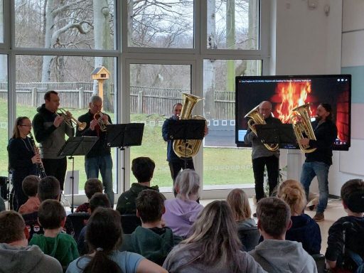 Musiker spielen Blechblasinstrumente vor einem Publikum in einem modernen Raum.
