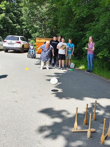Eine Gruppe von Kindern und Erwachsenen spielt eine Geschicklichkeitsübung im Freien.