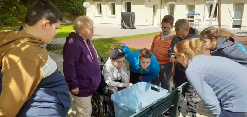 Gruppe von Menschen, die um einen Rollstuhl stehen und zusammen etwas betrachten.