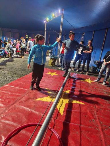 Junge geht auf einem Seil, während Zuschauer im Zirkuszelt zuschauen.
