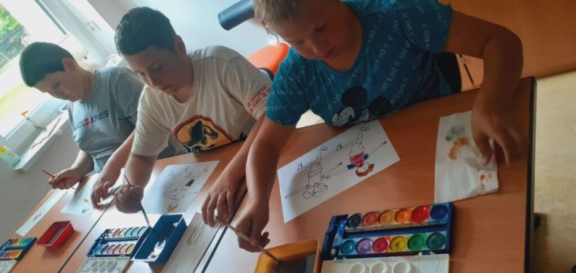 Drei Kinder sitzen an einem Tisch und malen mit Wasserfarben.