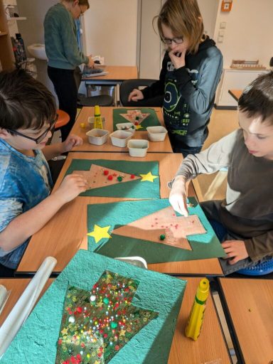 Kinder gestalten Weihnachtsbäume mit bunten Materialien am Tisch.