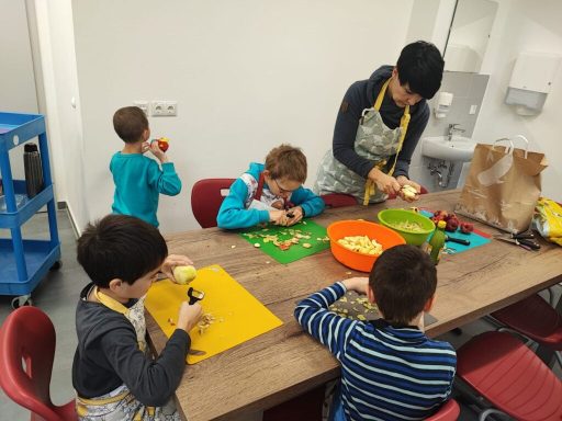 Kinder und Erwachsene schneiden Obst und Gemüse an einem Tisch in einer Küche.
