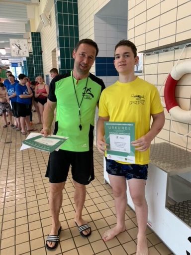 Ein Schwimmtrainer und ein Athlet halten Urkunden in einem Schwimmbad.