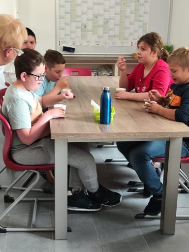 Sechs Kinder sitzen an einem Tisch und spielen gemeinsam mit Objekten.