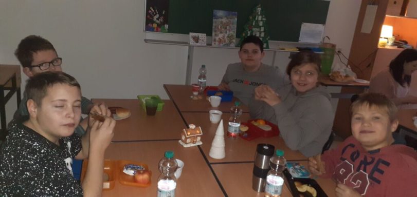 Fünf Kinder an einem Tisch, essen und lächeln in einem Klassenraum.