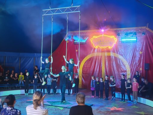 Drei Artisten zeigen Akrobatik an Schaukelringen in einem Zirkuszelt.