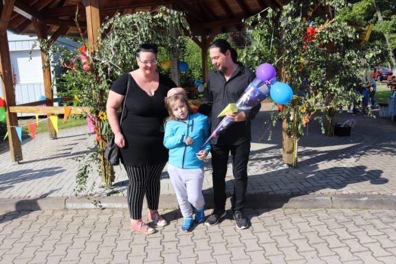 Familie steht zusammen unter einem Pavillon mit bunten Ballons und Dekorationen.