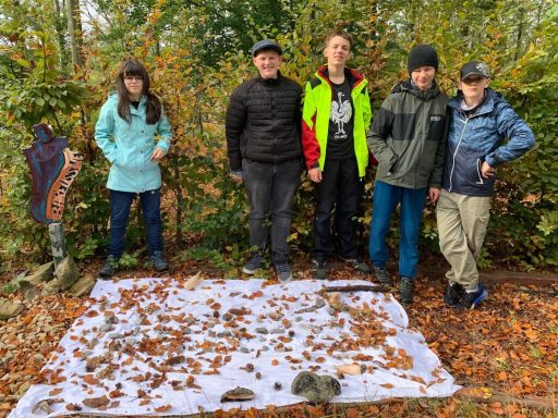 Fünf Personen stehen im Freien zwischen buntem Laub und Bäumen.