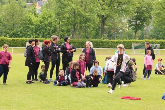 Gruppenaktivität im Freien mit Kindern und Erwachsenen auf einem Sportfeld.