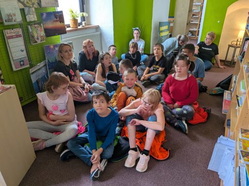 Gruppe von Kindern und Jugendlichen, die auf dem Boden in einem Raum sitzen.