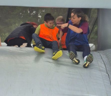 Kind in orange Weste sitzt auf einer großen, aufblasbaren Struktur, während eine Erwachsene hilft.