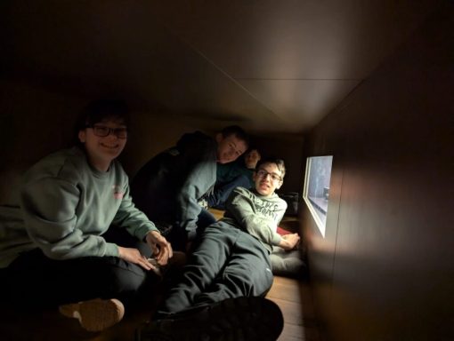 Drei Personen sitzen in einem engen Raum und schauen gemeinsam aus einem Fenster.