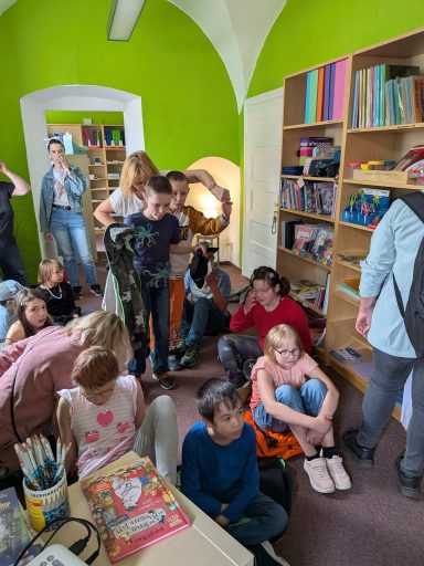 Gruppierung von Kindern und Erwachsenen in einem bunten Raum mit Regalen voller Bücher.