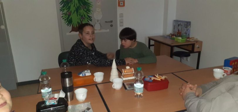 Zwei Kinder sitzen an einem Tisch, umgeben von Getränken und Snacks.