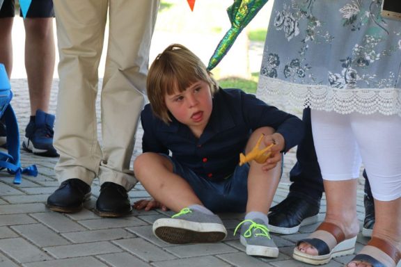 Ein Junge mit blonden Haaren sitzt auf dem Boden und hält ein Eis in der Hand.