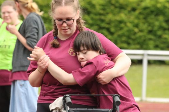 Eine Frau hilft einem Jungen mit Beeinträchtigung beim Sport auf dem Sportplatz.