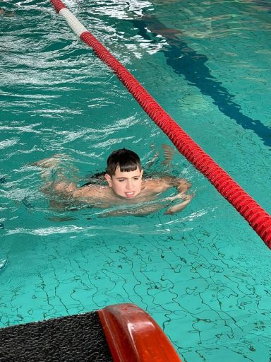 Junger Mann schwimmt im Becken, mit Fokus auf seinen Gesichtsausdruck im Wasser.