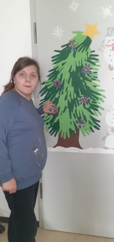 Mädchen steht neben einem selbstgemachten Weihnachtsbaum aus Papier an einer Tür.