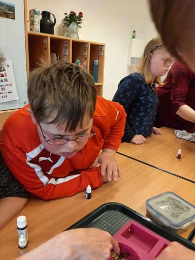 Ein Junge in einem roten Pullover konzentriert sich auf eine Aktivität am Tisch.