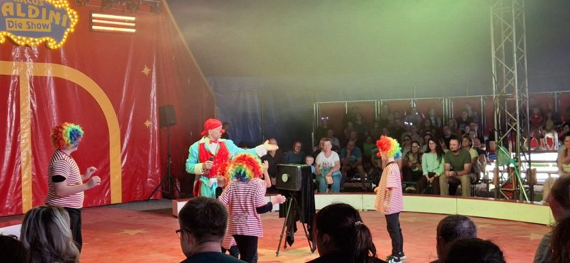 Clowns führen im Zirkus eine lustige Darbietung auf. Zuschauer beobachten begeistert.