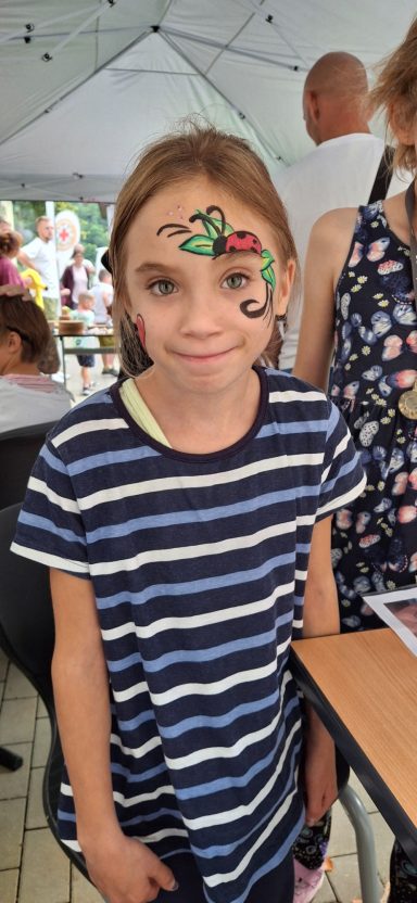 Mädchen mit gestreiftem Shirt und Gesichtsbemalung auf der Stirn, lächelnd.