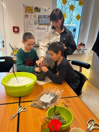 Drei Personen bei einer kreativen Bastelaktivität an einem Tisch mit Materialien.