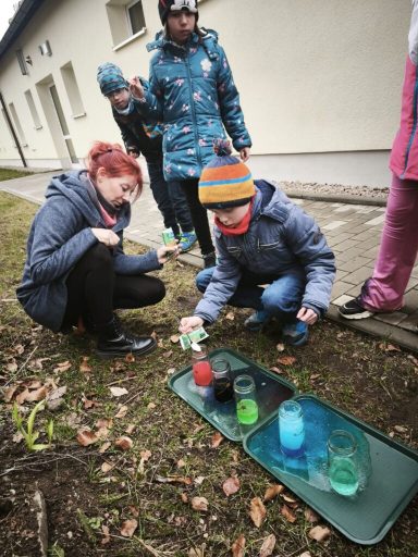 Kinder experimentieren im Freien mit bunten Flüssigkeiten in Gläsern.