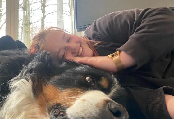 Eine lachende Person liegt mit ihrem Kopf auf einem großen Hund.