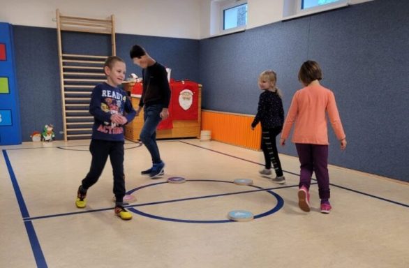 Vier Kinder spielen in einem Raum, um einen blauen Kreis auf dem Boden.