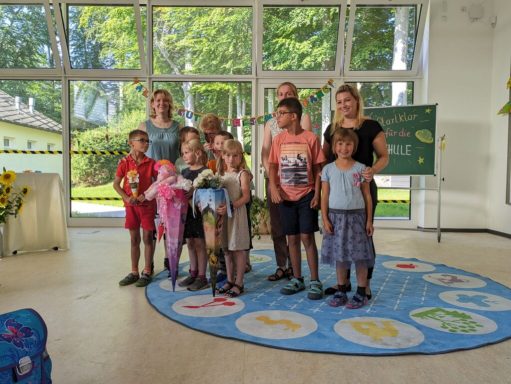 Gruppe von Kindern und Erwachsenen in einem Raum mit bunten Dekorationen und Teppich.