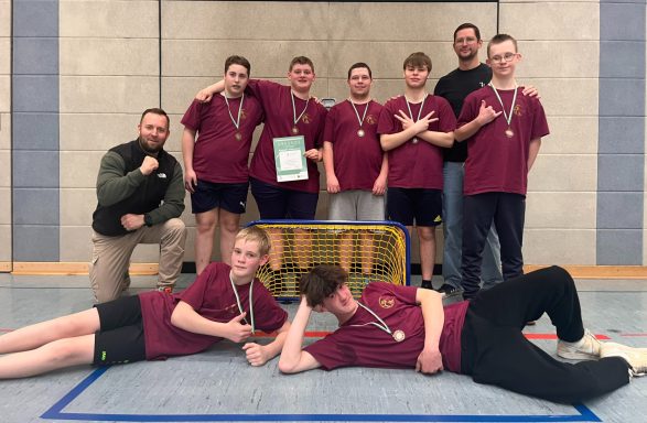 Eine Gruppe junger Menschen in roten T-Shirts posiert mit Medaillen und Pokal.