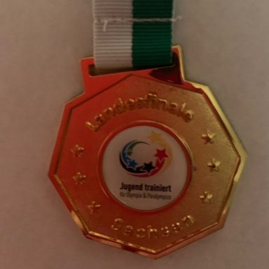 Goldene Medaille mit grünem Band, geprägt mit Symbolen von Landesspielen.