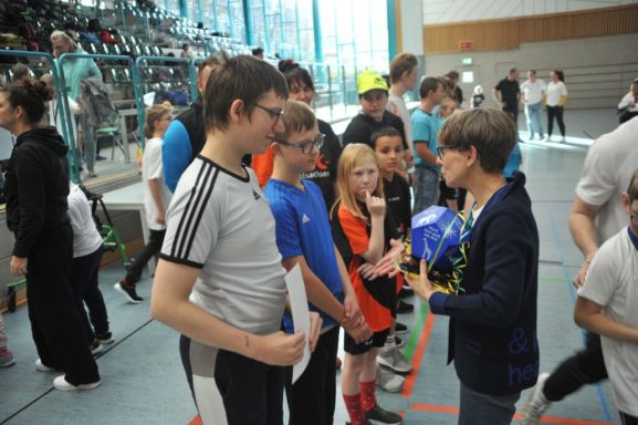 Gruppe von Jugendlichen in Sportkleidung bei einer Veranstaltung, die mit einer Erwachsenen spricht.