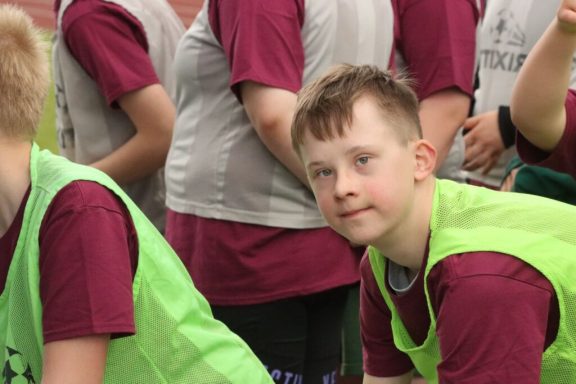 Ein Junge in einem grünen Weste blickt lächelnd zur Kamera während einer Sportaktivität.