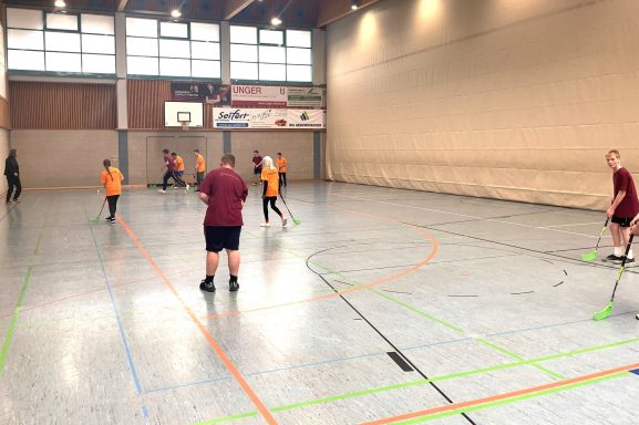 Gruppenspiel in einer Sporthalle mit Kindern in orange und Betreuern in rot.