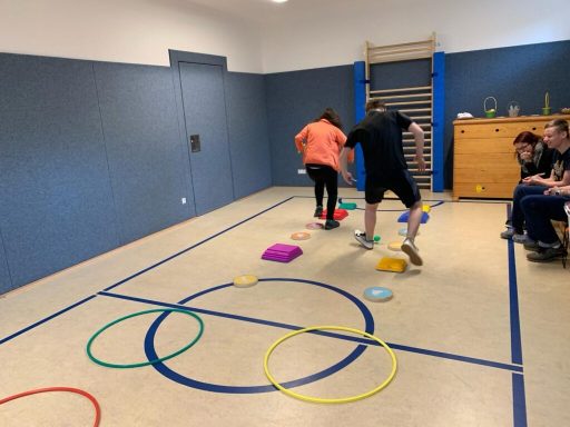 Zwei Personen überwinden Hindernisse auf einem turnerfreundlichen Boden mit bunten Matten.