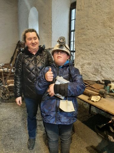 Ein Junge in Helm mit Daumen hoch neben einem Mann in schwarzer Jacke.