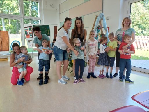 Eine Gruppe von Kindern und Erwachsenen steht lächelnd in einem hellen Raum.