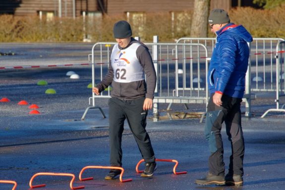 Ein Trainer beobachtet einen Sportler beim Training mit Hürden auf einer Eisfläche.
