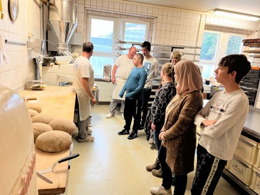 Eine Gruppe von Menschen beobachtet einen Bäcker in einer Backstube.