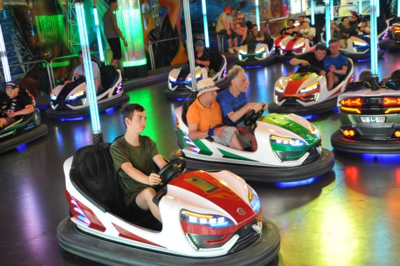 Autoscooter mit Fahrern in einer bunten, beleuchteten Umgebung.