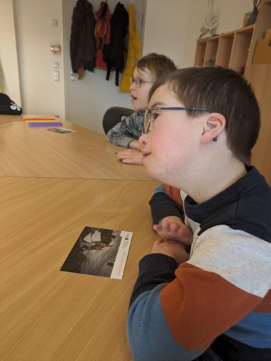 Zwei Kinder sitzen an einem Tisch und schauen auf ein Foto, das vor ihnen liegt.