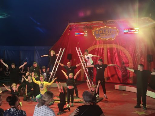 Kinder führen in einem Zelt eine Zirkusaufführung mit Akrobatik und Props auf.