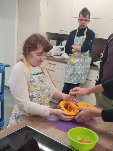 Zwei Personen kochen zusammen in einer modernen Küche, eine Person hält eine Schüssel mit Kürbis.