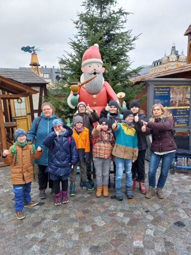 Gruppe von Kindern und Erwachsenen posiert vor einem großen Weihnachtsmann.
